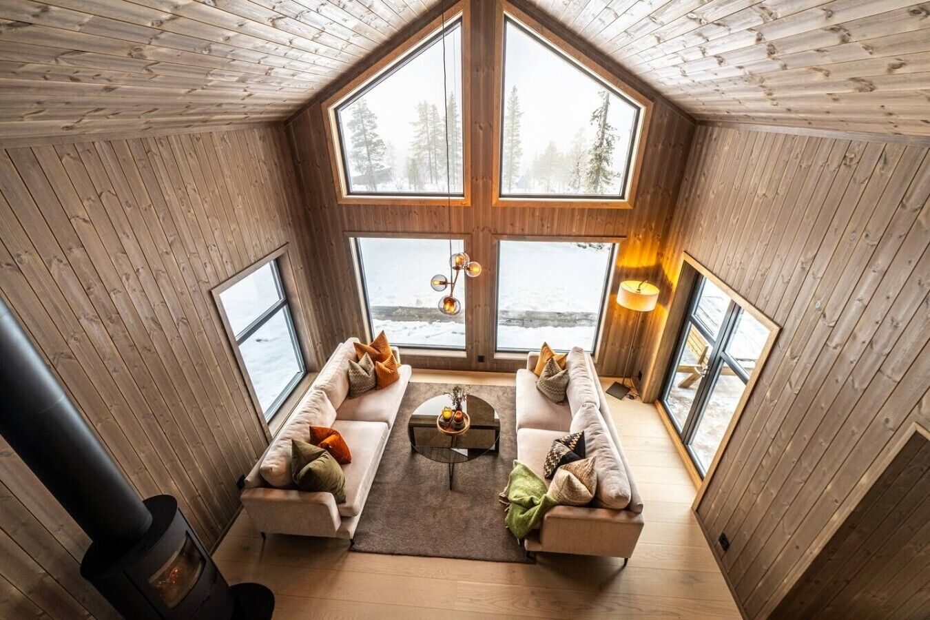 A cozy cabin interior with a large window, a fireplace, and a sofa set.