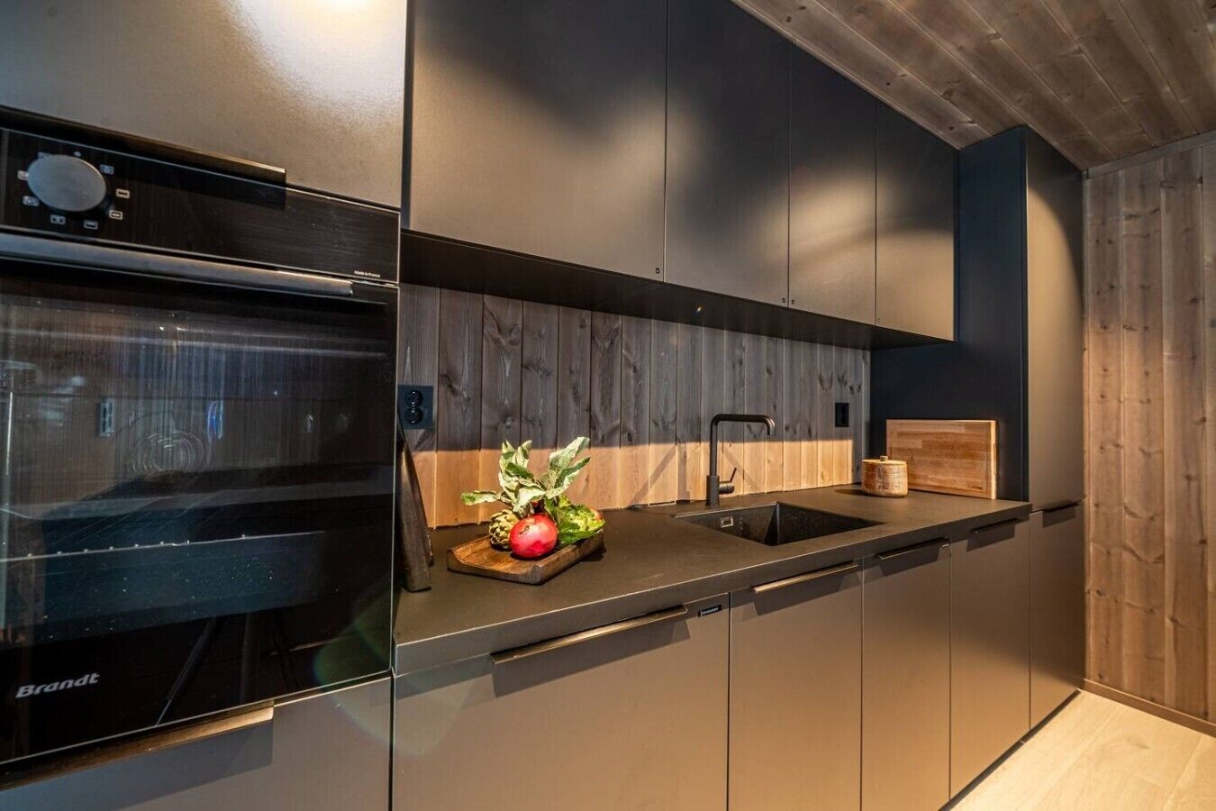 A modern kitchen with a built-in oven, a sink, and a wooden backsplash.