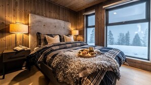 A cozy bedroom with a large bed, wooden walls, and a view of a snowy landscape through a large window.