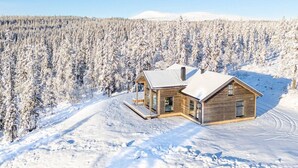 A wooden cabin with a snow-covered roof, surrounded by a dense forest.
