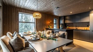 A modern dining area with a long table set for a meal, wooden walls, and a kitchen in the background.