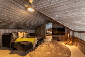 A cozy attic bedroom with a bed, a television, and a fireplace.