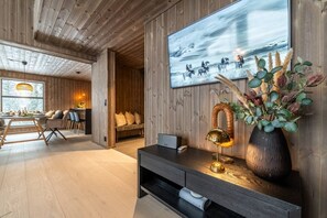 A modern interior with a wooden ceiling, a dining area with a table and chairs, a sofa, and a wall-mounted TV.