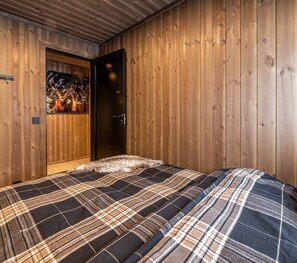 A room with wooden panel walls, a bed with a plaid bedspread, and a door with a deer head decoration.