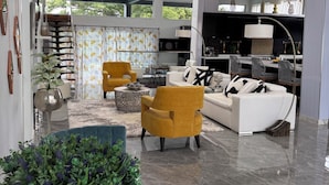 A spacious living area with a high ceiling, a staircase, and a kitchen area. - Villa Near Negril | 5BR Private Pool & Spa | Caribbean Family & Group Retreat (LITTLE LONDON)