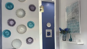 A modern interior with a black leather sofa, decorative wall plates, a blue accent wall, and a glass door with a blue vase. - Villa Near Negril | 5BR Private Pool & Spa | Caribbean Family & Group Retreat (LITTLE LONDON)