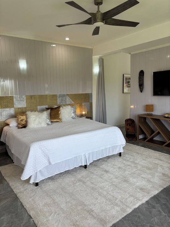 Un dormitorio con una cama grande, un ventilador de techo, un televisor y un panel decorativo en la pared.
