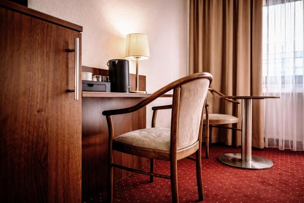 Ein Hotelzimmer mit einem Holzschrank, einem Schreibtisch mit Lampe, einem Stuhl und einem runden Tisch.