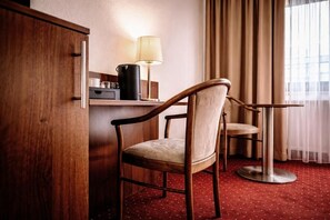 Une chambre d’hôtel avec une armoire en bois, un bureau avec une lampe, une chaise et une table ronde.