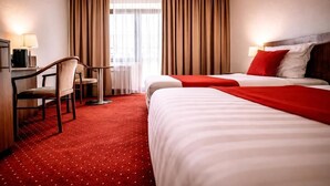 A hotel room with two beds, a desk, a chair, and a window with curtains. - REDBERRY Hotel - Düsseldorf - Neuss (Neuss)