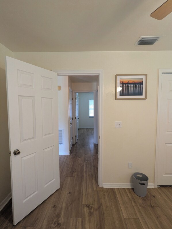 A hallway with wooden flooring, white doors, and a framed picture on the wall.