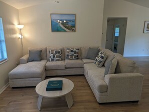 A living room with a sectional sofa, a round coffee table, and a painting on the wall.