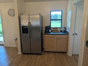 A kitchen with a stainless steel refrigerator, wooden cabinets, a window with a view, and a clock on the wall.