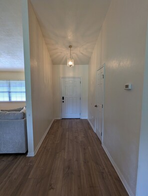 A hallway with wooden flooring, white walls, a white door at the end, and a ceiling light fixture.