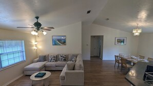 A spacious living room with a sectional sofa, a dining area with a long table, and a kitchen counter.