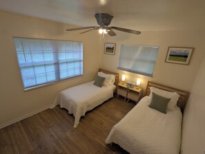 A bedroom with two single beds, a ceiling fan, and two bedside tables with lamps.
