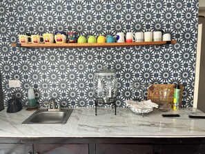 Een keuken met een decoratieve spatwand, een marmeren aanrecht, een plank met mokken, een blender en een mand.