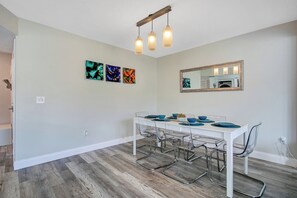 A dining area with a white table, blue plates, and clear chairs. There are three abstract paintings on the wall and a mirror above the table. - Disney-Themed Family Home, Pool and Courts, Minutes to the Parks (Davenport)