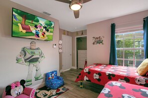 A bedroom with a TV, a ceiling fan, a window with curtains, a door, and a Mickey Mouse themed bedspread. - Disney-Themed Family Home, Pool and Courts, Minutes to the Parks (Davenport)