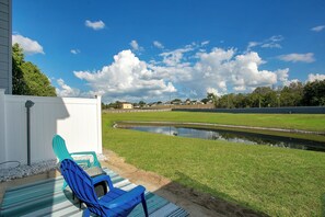A patio with a blue chair and a striped mat, a white fence, a grassy area, and a body of water. - Disney Area · Themed Family Home · Pool · Parking (Davenport)