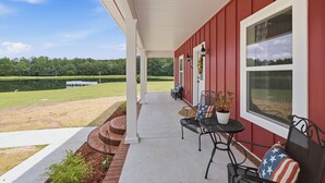A covered patio with outdoor furniture, a view of a lake, and a red building.