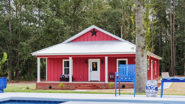 A red building with a white porch and a pool in the foreground.