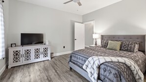 A bedroom with a bed, a TV, a ceiling fan, and a nightstand. - Come stay at peaceful Timberland Cottage, a fully furnished 3 bedroom property. (Claxton)