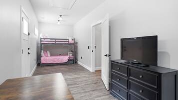 Quarto com uma cama beliche, televisão sobre uma cômoda e mesa de madeira.