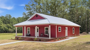A red single-story house with a covered porch and a metal roof. - Come stay at peaceful Timberland Cottage, a fully furnished 3 bedroom property. (Claxton)