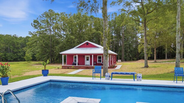 A swimming pool with a red building in the background. - Come stay at peaceful Timberland Cottage, a fully furnished 3 bedroom property. (Claxton)
