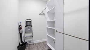 A clean, white closet with open shelves and a vacuum cleaner.