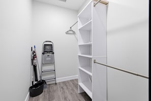 A clean, white closet with open shelves and a vacuum cleaner.