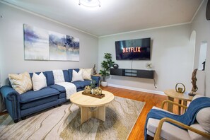 A living room with a blue sofa, a coffee table, a TV mounted on the wall, and a plant.