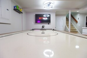 A room with a large, flat-screen TV mounted on the wall displaying the Netflix logo, a ping pong table in the center, and a staircase leading to another level.