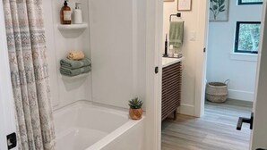 A bathroom with a bathtub, shower, and a small shelf with toiletries. - Fabulous 2-bedroom apartment in Traverse City-Monthly Rental (Traverse City)