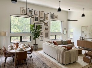 A modern living room with a dining area, large windows, and a variety of framed pictures on the wall. - Fabulous 2-bedroom apartment in Traverse City-Monthly Rental (Traverse City)