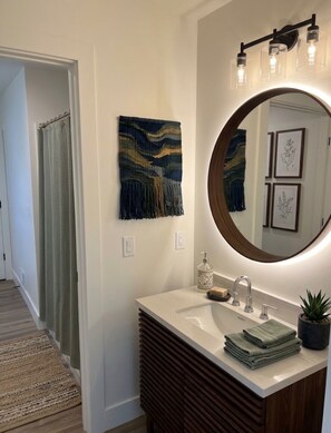 A bathroom with a round mirror, a sink, a towel rack, and a decorative wall piece. - Fabulous 2-bedroom apartment in Traverse City-Monthly Rental (Traverse City)