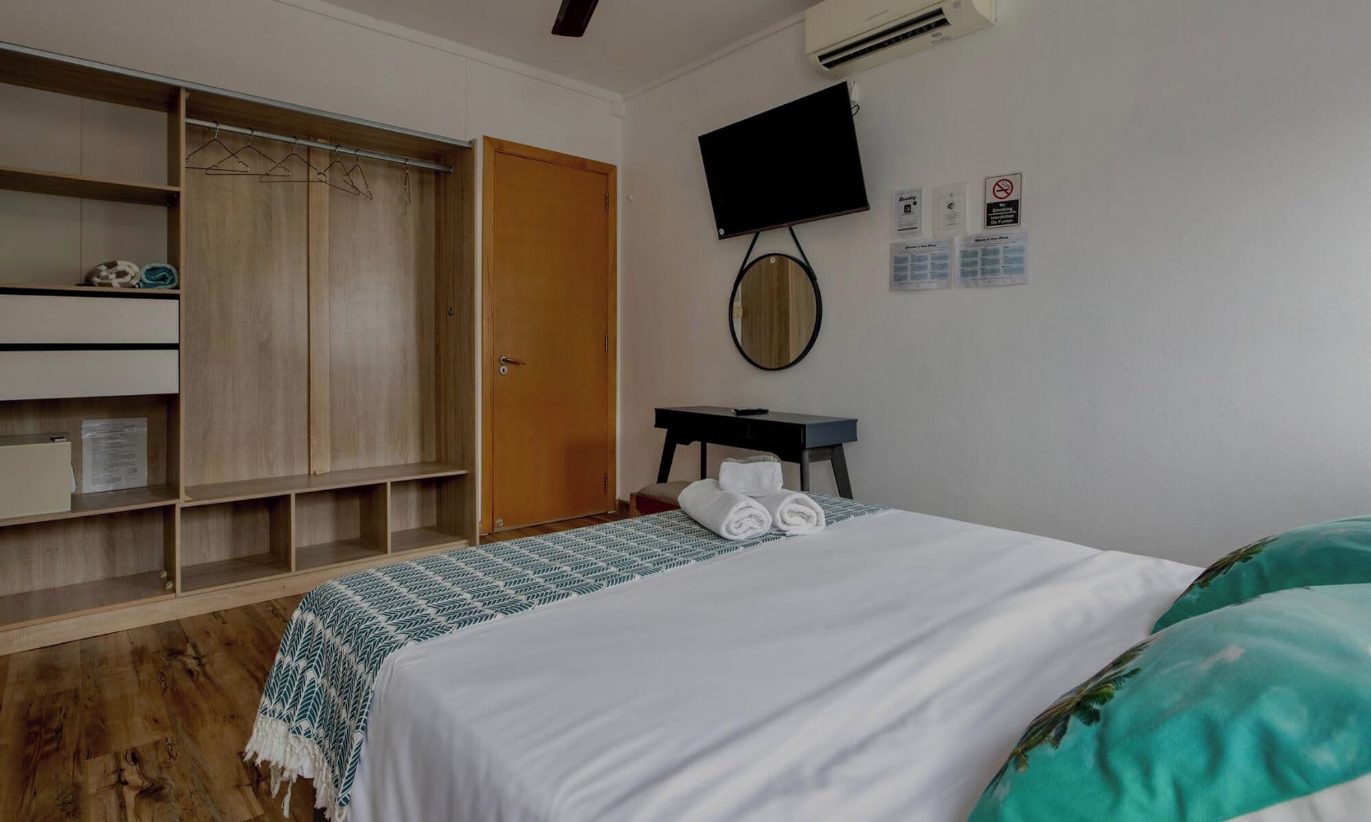 Une chambre d’hôtel équipée d’un lit, d’une armoire, d’un bureau, d’une télévision et d’un miroir.