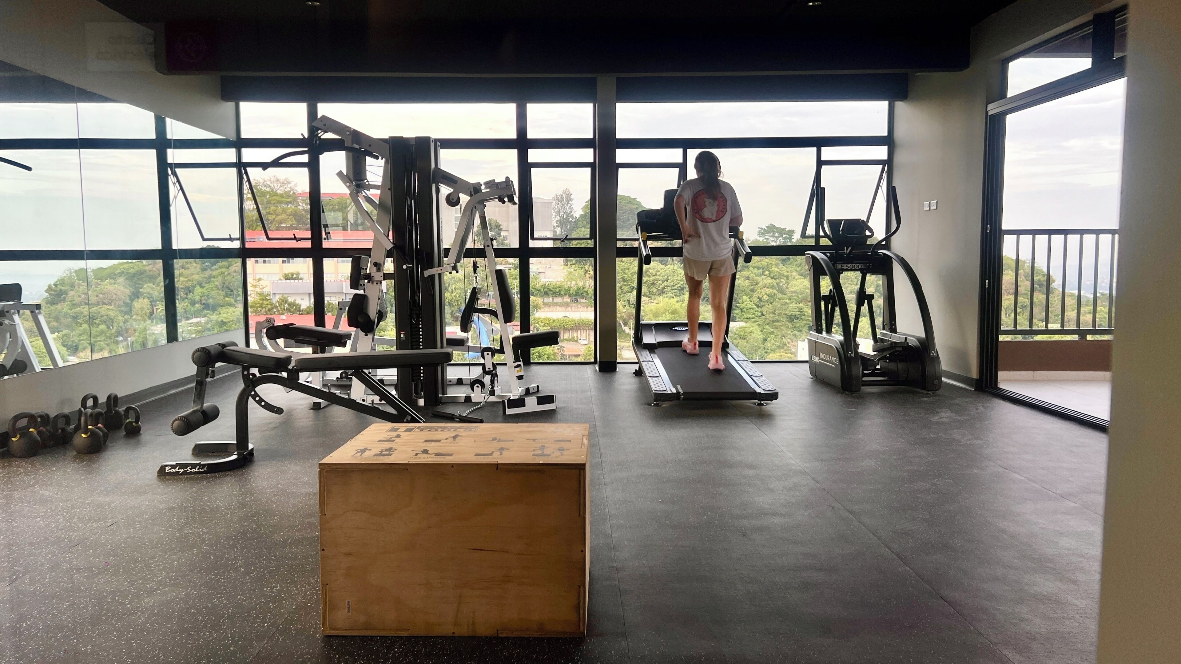 A gym with exercise equipment, a wooden box, and a person using a treadmill.