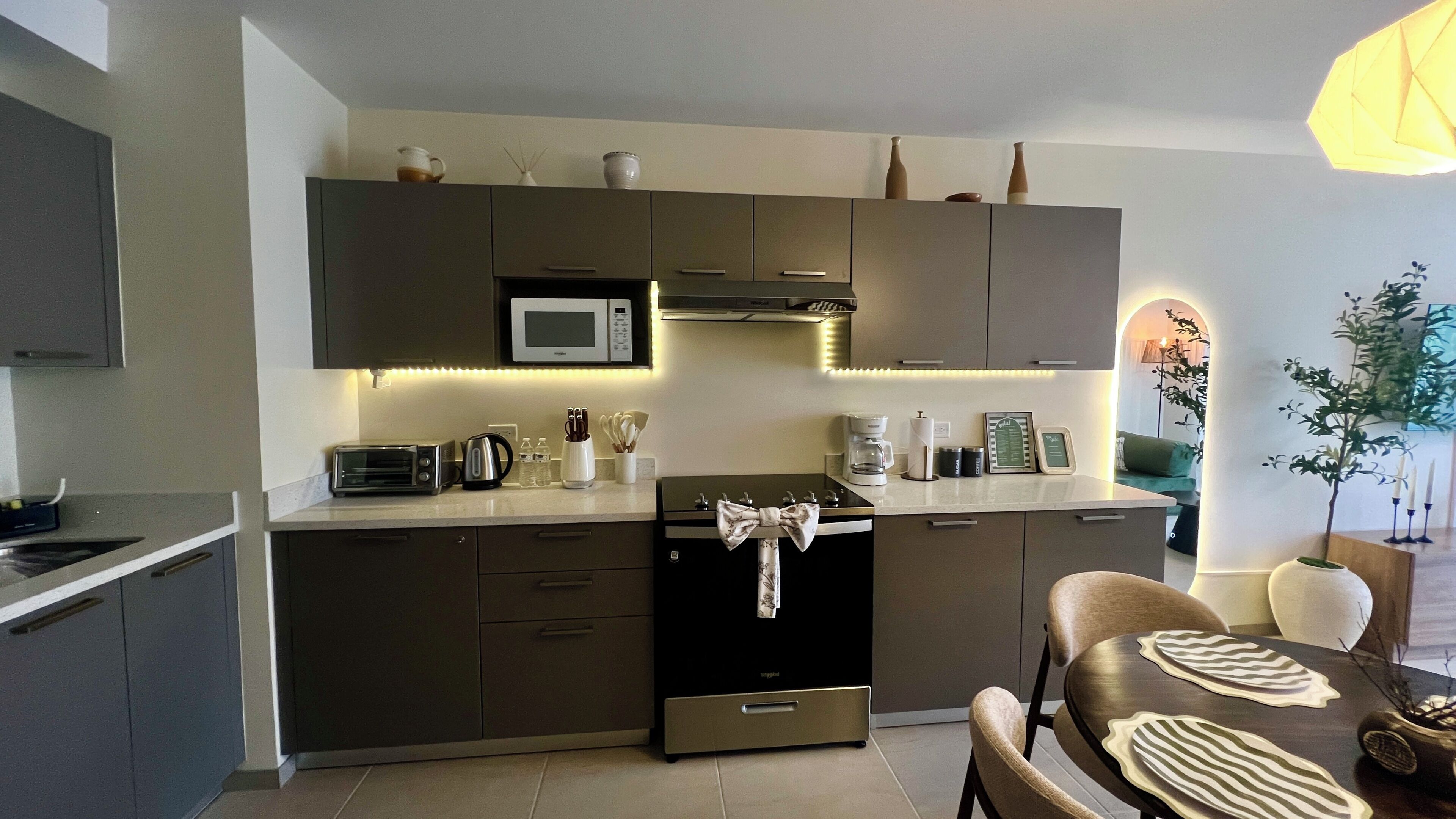 A modern kitchen with a microwave, toaster, and coffee maker. There is a dining table with a decorative bow tie and a vase with branches.