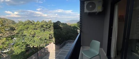 A balcony with a view of a lush green landscape, a tiled floor, and a single chair.