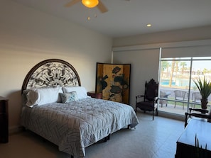 Ein Schlafzimmer mit einem großen Bett, einem Deckenventilator, einem Gemälde und Blick ins Freie.