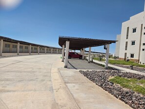 A parking area with a covered carport, a red car, and a building with multiple windows. - 3 Bdrm 3 Bath 1st Flr condo Mayan Lakes. Access to the Mayan Palace. Pets yes! (Mayan Lakes)