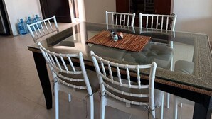 A dining area with a glass-top table, white chairs, a dark wooden cabinet, and a door leading to another room.