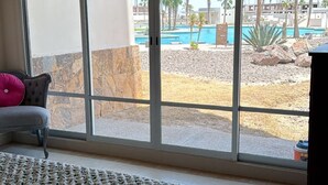 A bedroom with a large window, a bed with a patterned bedspread, a chair, and a view of an outdoor pool area.