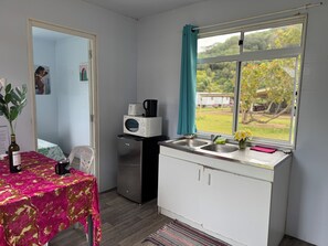 A compact kitchenette with a microwave, toaster, and coffee maker on the countertop, a sink, and a window with a view of greenery. - VAI Bungalow with beach access, kayaks, and a relaxation area by the lagoon (MOOREA Haapiti)