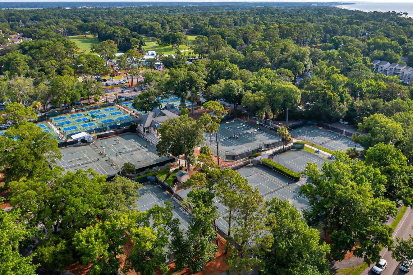 Vista aérea de una zona residencial con múltiples canchas de tenis, rodeada de abundante vegetación y un campo de golf al fondo.