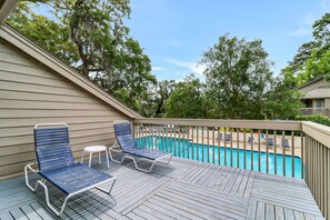 A wooden deck with two lounge chairs and a small table, overlooking a swimming pool. - Island Ease Villa Golf, Beach, Marina Nearby (Hilton Head Island)