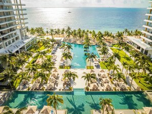 A resort with a central swimming pool surrounded by lounge chairs and palm trees, overlooking a beach and ocean. - Garza Blanca Resort & Spa with AC in peaceful Cancún for a relaxing getaway (Cancún)