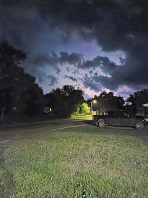A grassy area with a vehicle parked on the side of a road, under a cloudy sky. - Beautiful Viking "Long Hall" lodge with AC in charming Waubay SD. (Waubay)